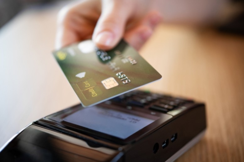 a hand holding a payment card towards a card reader machine to make a donation
