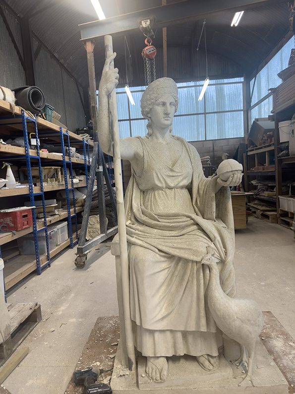 A stone sculpture of the goddess Juno, seated with a peacock beside her. She holds an orb and stave